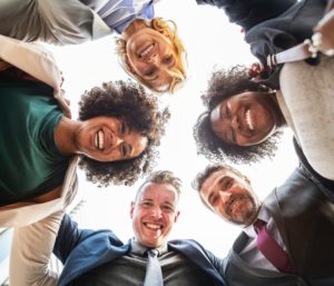 A group of people linked in a circle, smiling, 2 men, 3 women, taken from below