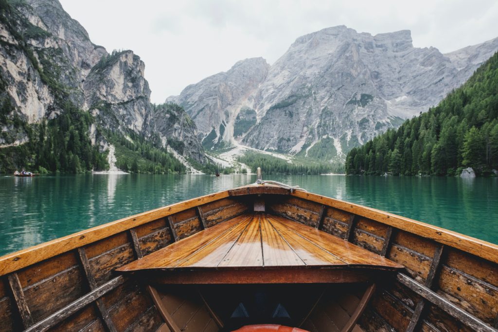 sitting in a wooden rowing boat, looking out over the front, at a green body of water and rocky mountains ahead. A sense of adventure or exploration.